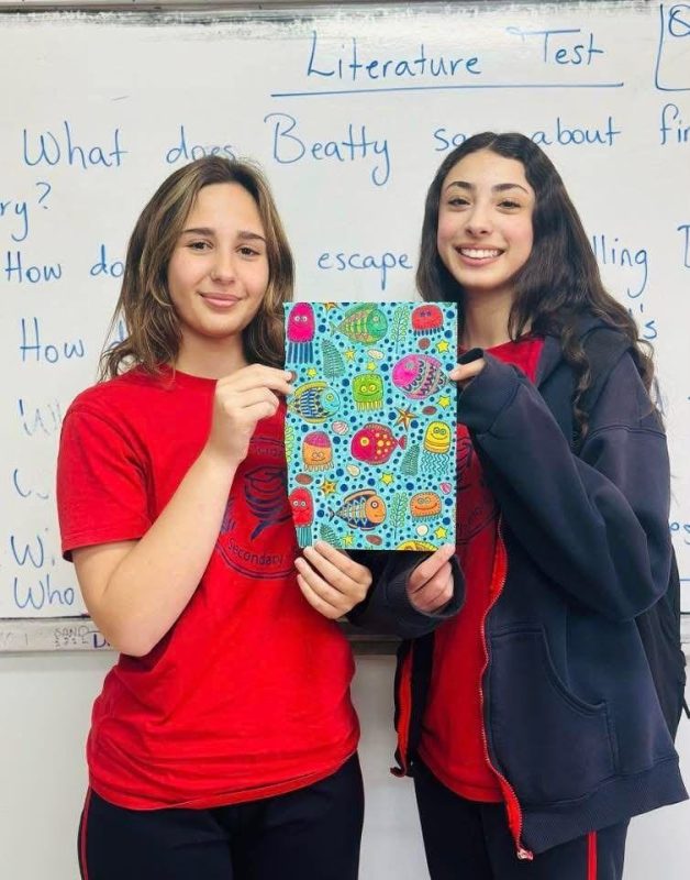 Two students hold a book in front of a “Literature Test” board