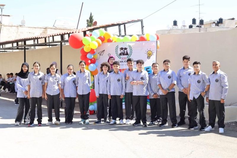 طلاب بالزي المدرسي يصطفّون أمام لافتة الترحيب والبالونات