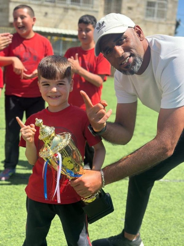 A young student holds a trophy beside his smiling coach
