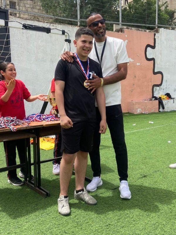 A student with a medal stands with his coach on the sports field