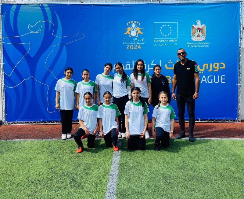 فريق كرة القدم للطالبات ومدرّبه أمام لافتة دوري 2024