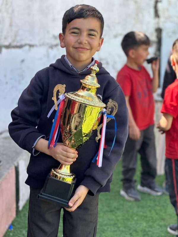 A student holds a large trophy on the sports field